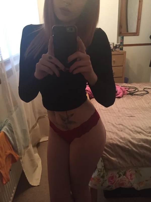 Personne prenant un selfie dans un miroir, haut noir, sous-vêtements rouges, tatouage au ventre, chambre, lumière naturelle
