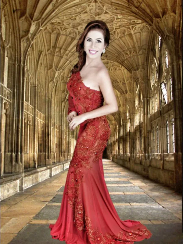 Femme en robe rouge longue posant dans un couloir gothique à voûtes en pierre.